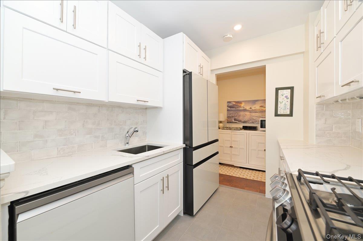 320 East Shore Road, Unit 4C Great Neck, NY 11023 - Photo 13 of 31 Kitchen featuring stainless steel appliances, light stone countertops, decorative backsplash, white cabinetry, and recessed lighting