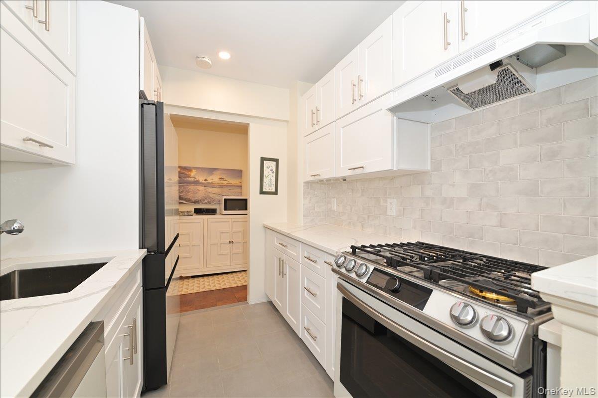 320 East Shore Road, Unit 4C Great Neck, NY 11023 - Photo 14 of 31 Kitchen with stainless steel appliances, under cabinet range hood, white cabinets, and light stone counters