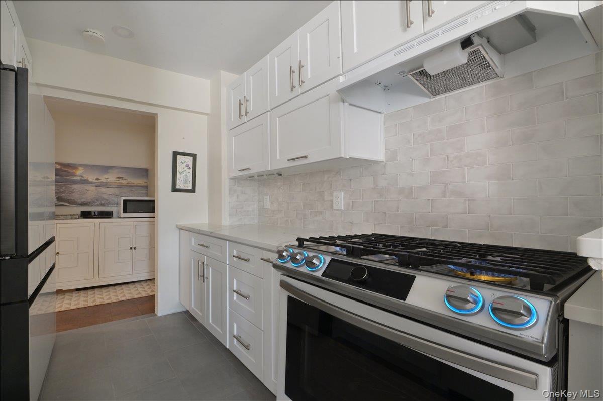 320 East Shore Road, Unit 4C Great Neck, NY 11023 - Photo 17 of 31 Kitchen featuring appliances with stainless steel finishes, white cabinets, under cabinet range hood, light stone countertops, and decorative backsplash
