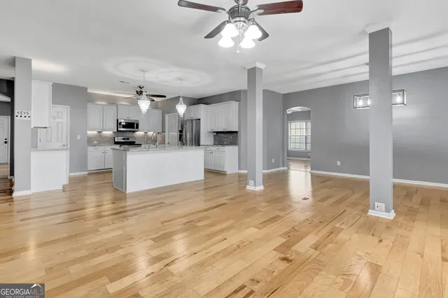 a view of an empty room with wooden floor fan and windows