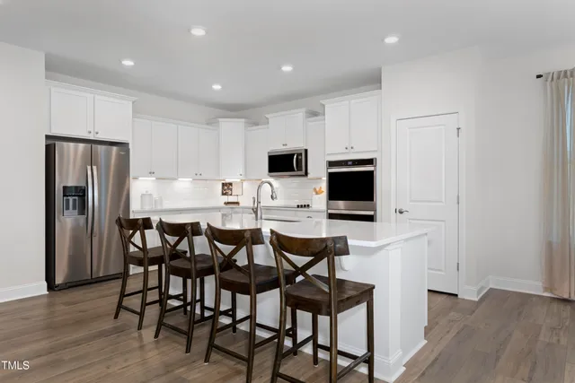 a kitchen with stainless steel appliances a dining table chairs microwave and refrigerator