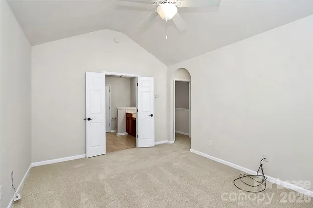 an empty room with a chandelier fan and kitchen view