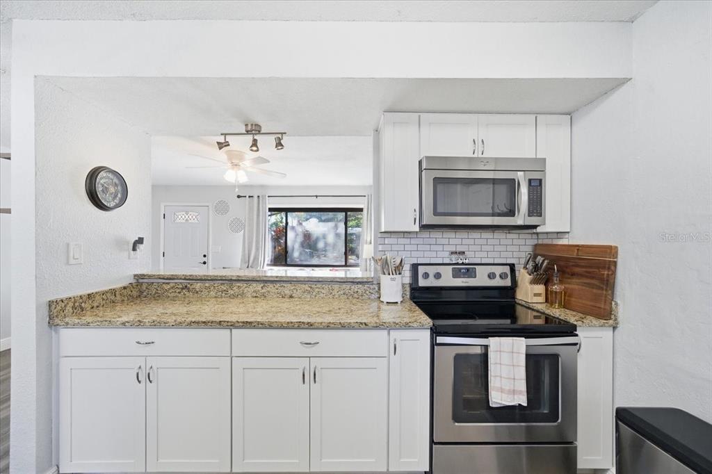 3487 Begonia Place Largo, FL 33771 - Photo 15 of 34 a kitchen with stainless steel appliances granite countertop a stove a microwave and white cabinets