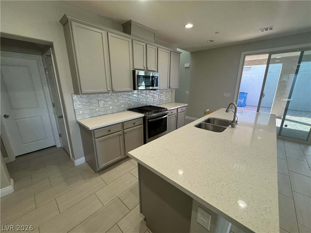 1051 East Sunset Road Henderson, NV 89011 - Photo 7 of 36 Kitchen featuring stainless steel appliances, gray cabinets, decorative backsplash, light stone countertops, and an island with sink