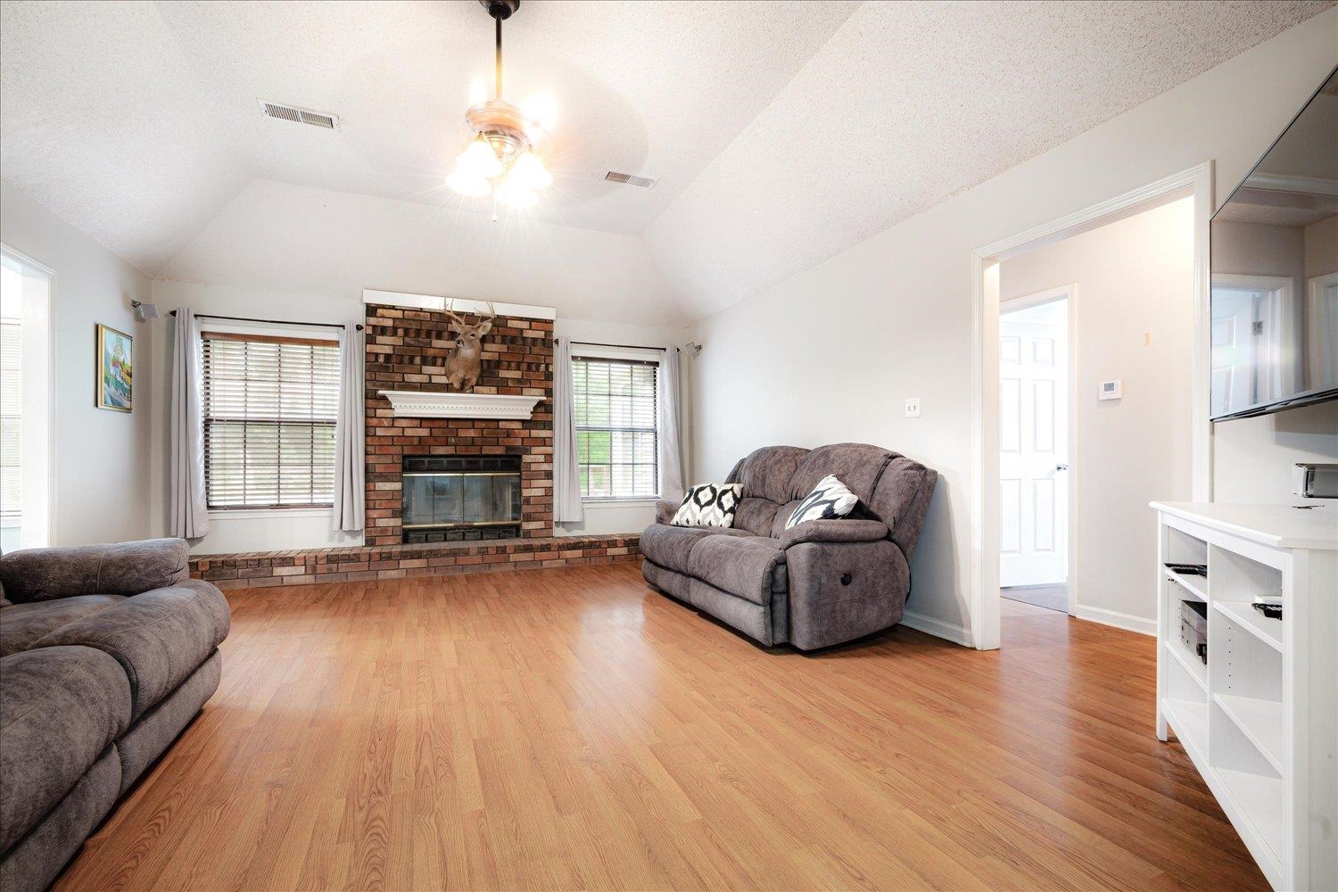Living room featuring ceiling fan, light wood-type flooring, vaulted ceiling, and a brick fireplace