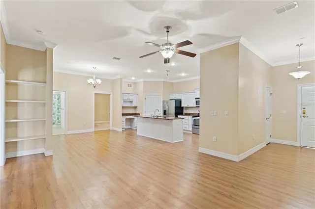 a view of an empty room and kitchen view with wooden floor
