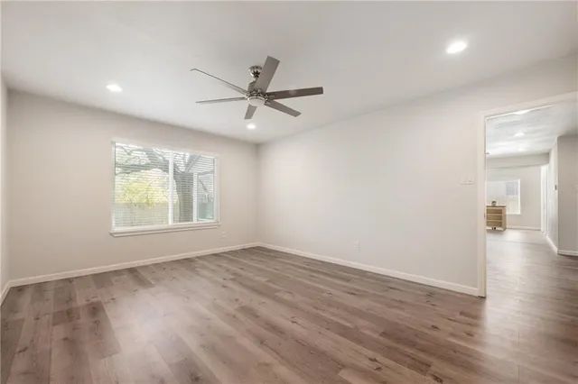 an empty room with wooden floor fan and windows