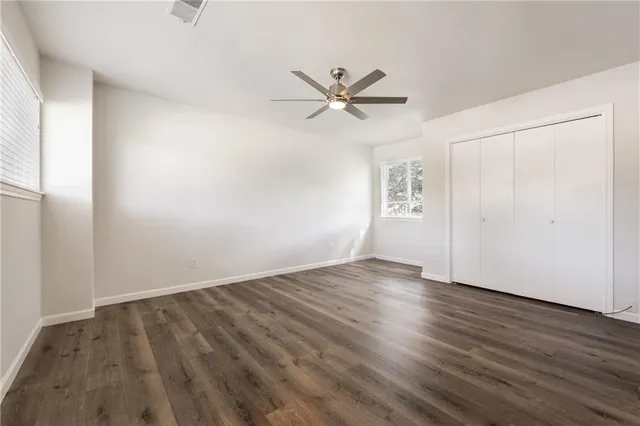 an empty room with wooden floor fan and windows