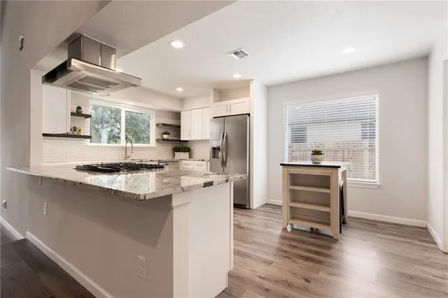 a kitchen with stainless steel appliances kitchen island granite countertop a refrigerator a sink dishwasher a stove and a refrigerator