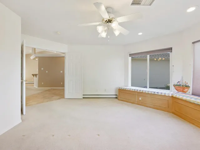 an empty room with chandelier fan and windows