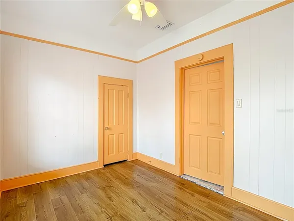an empty room with wooden floor fan and windows