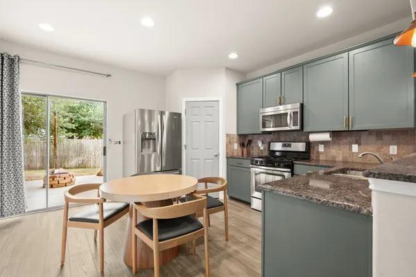 a kitchen with stainless steel appliances granite countertop a stove top oven a sink dishwasher a dining table and chairs with wooden floor