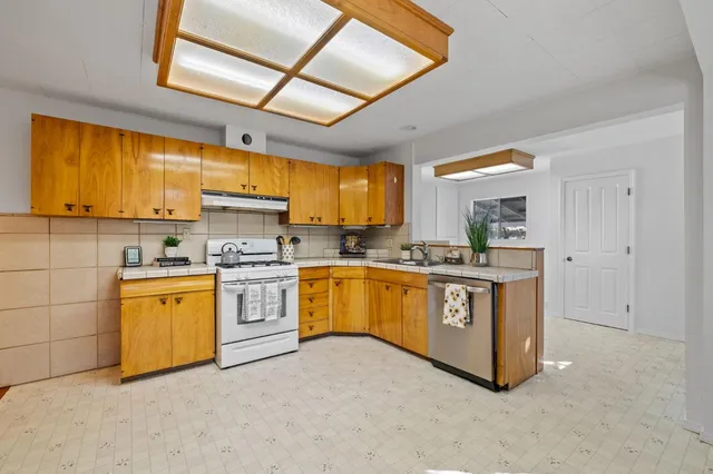 a large kitchen with stainless steel appliances granite countertop a stove a sink dishwasher and white cabinets with wooden floor