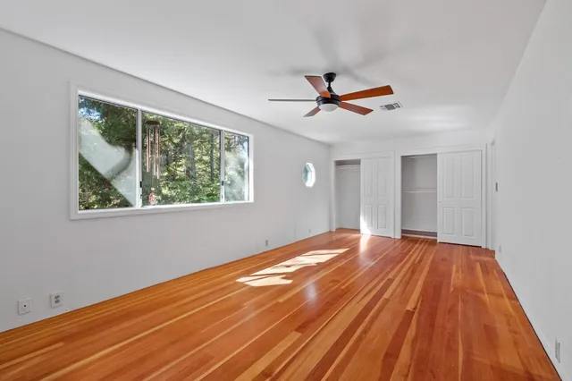 a view of empty room with wooden floor and fan