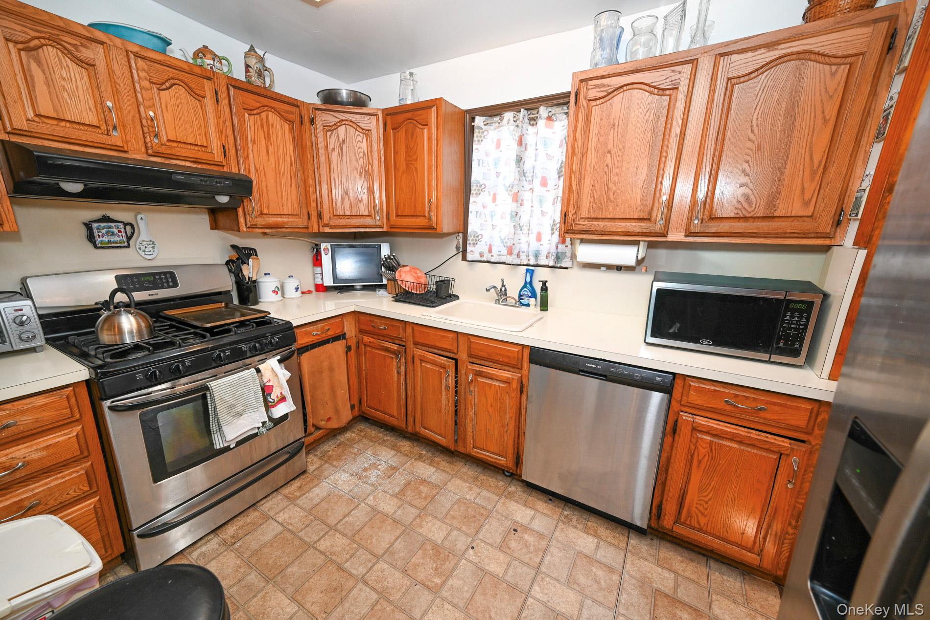 165 Cochran Place Valley Stream, NY 11581 - Photo 7 of 25 Kitchen with stainless steel appliances, brick patterned floors, brown cabinetry, and light countertops