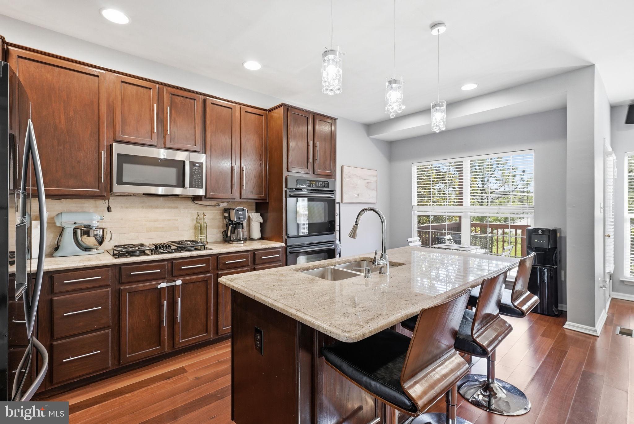 14231 Hunters Run Way Gainesville, VA 20155 - Photo 3 of 41 a kitchen with stainless steel appliances granite countertop a stove top oven a sink dishwasher a dining table and chairs with wooden floor
