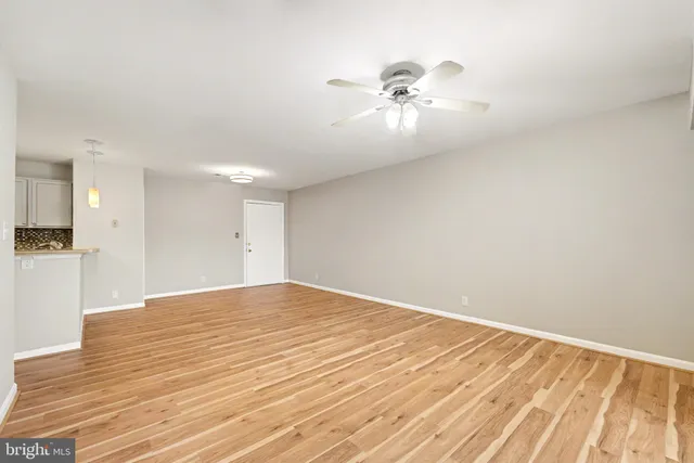 a view of an empty room with wooden floor and a ceiling fan