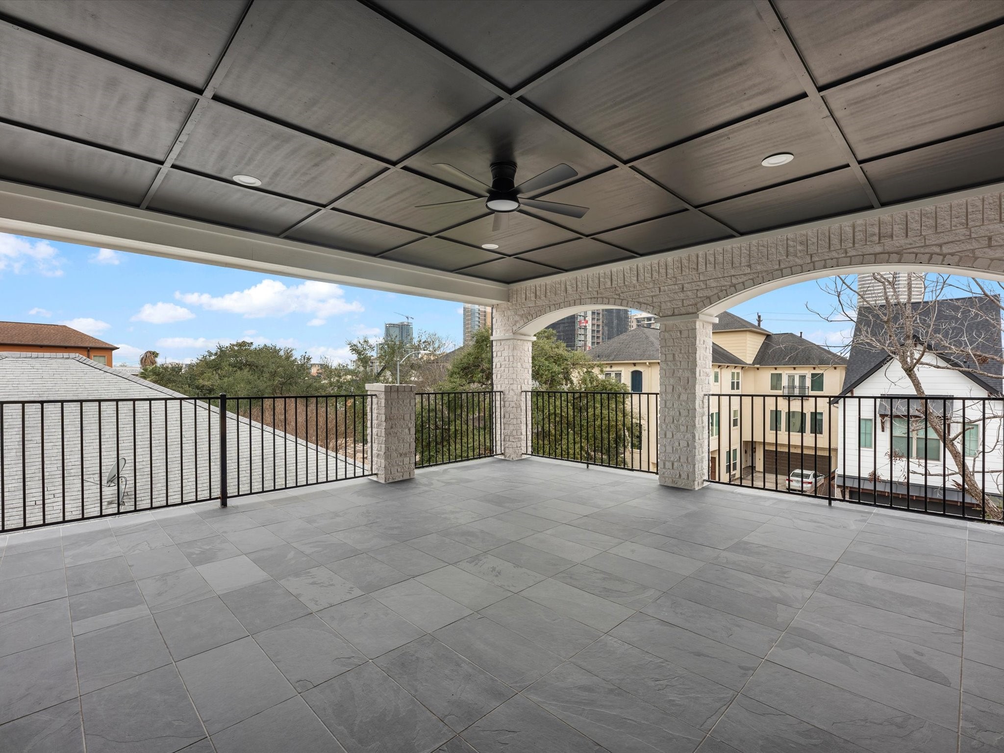 1319 West Bell Street Houston, TX 77019 - Photo 44 of 50 This spacious covered terrace features a sleek tiled floor and ceiling fan, offering a comfortable outdoor entertainment space. The view includes neighboring homes and greenery, creating a serene environment.