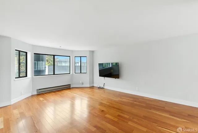 a view of an empty room with wooden floor and a window