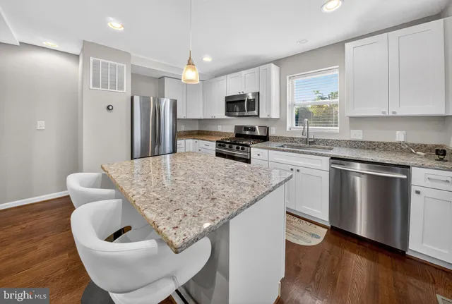 a kitchen with stainless steel appliances granite countertop a kitchen island hardwood floor sink stove and white cabinets