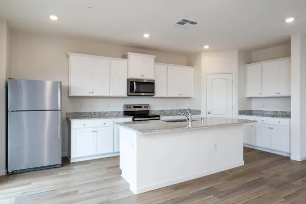 a kitchen with stainless steel appliances granite countertop a refrigerator a sink dishwasher a stove top oven a refrigerator and white cabinets with wooden floor
