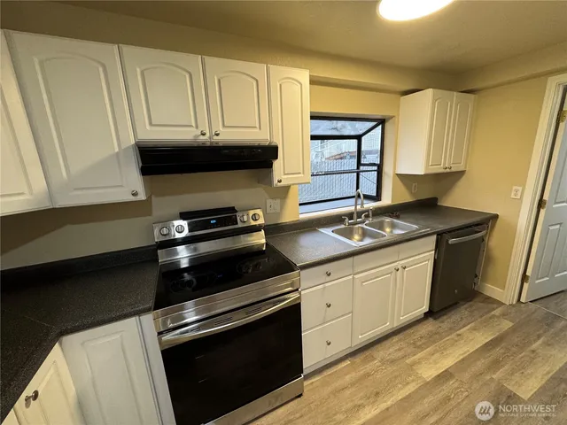 a kitchen with granite countertop a sink dishwasher stove and cabinets