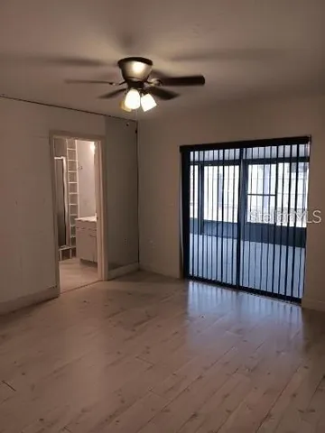 a view of an empty room with wooden floor and fan
