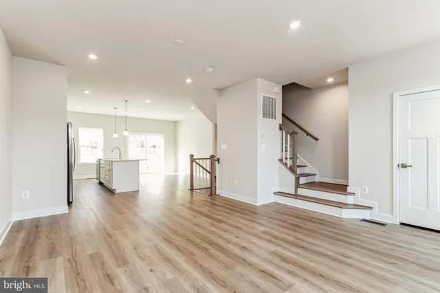 a view of an empty room with wooden floor and a kitchen