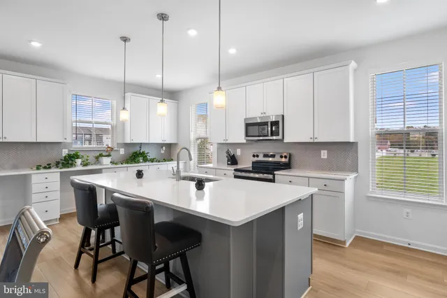 a kitchen with stainless steel appliances kitchen island a white table chairs and a window