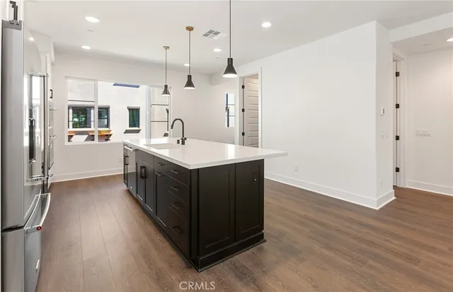 a kitchen with stainless steel appliances granite countertop a refrigerator a oven a sink and white cabinets with wooden floor