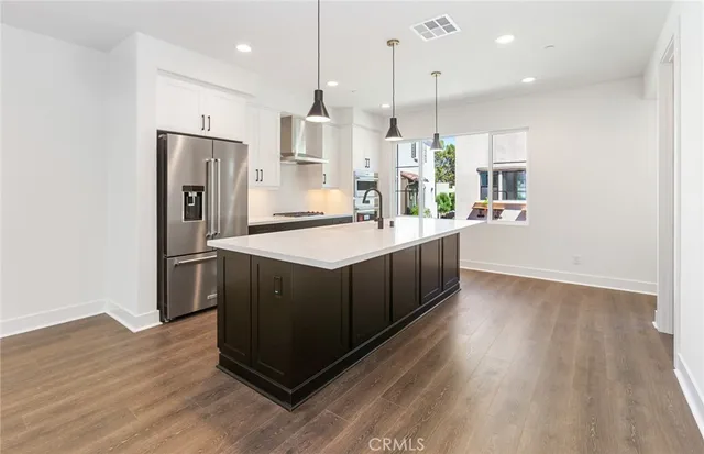 a kitchen with stainless steel appliances kitchen island granite countertop a refrigerator a stove and a wooden floors