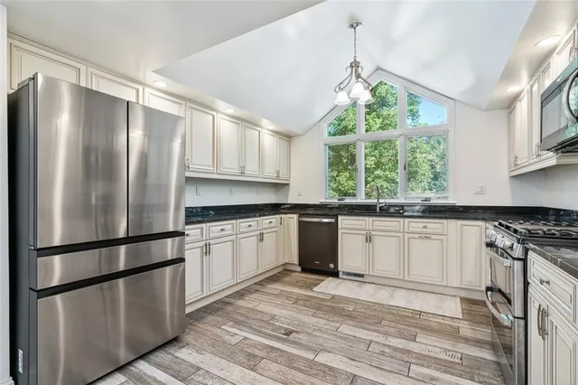 a kitchen with stainless steel appliances granite countertop a refrigerator a sink dishwasher a stove and white cabinets with wooden floor