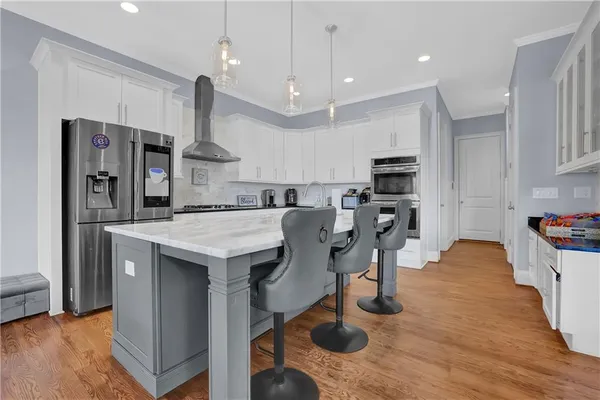 a kitchen with stainless steel appliances kitchen island granite countertop a stove a refrigerator a oven a sink a dining table and chairs with wooden floor