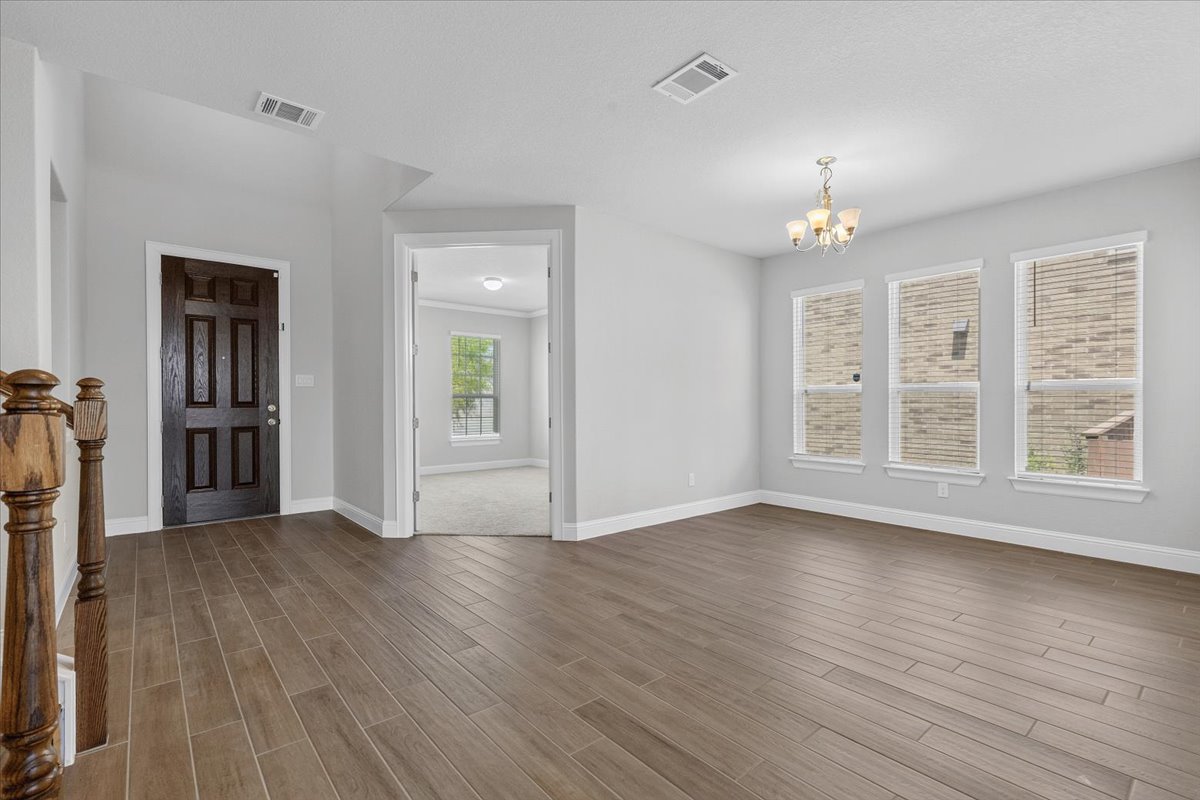 Natural light floods this versatile living area, featuring rich wood-look flooring and a chandelier for elegant illumination.