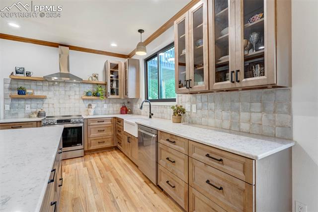 20880 Scott Road Peyton, CO 80831 - Photo 8 of 49 Kitchen featuring decorative backsplash, light wood-type flooring, wall chimney exhaust hood, appliances with stainless steel finishes, and decorative light fixtures