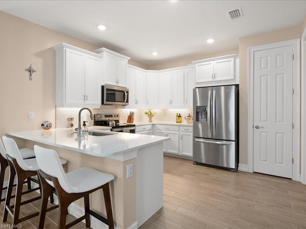 1046 Enbrook Loop Naples, FL 34114 - Photo 3 of 43 Kitchen with kitchen peninsula, sink, white cabinets, and appliances with stainless steel finishes