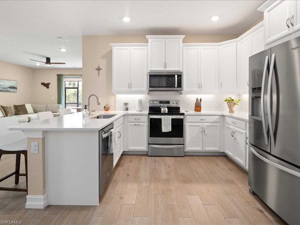 1046 Enbrook Loop Naples, FL 34114 - Photo 4 of 43 Kitchen with sink, kitchen peninsula, light hardwood / wood-style floors, a breakfast bar, and appliances with stainless steel finishes