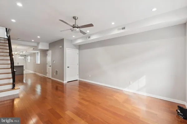 an empty room with wooden floor a ceiling fan and kitchen view