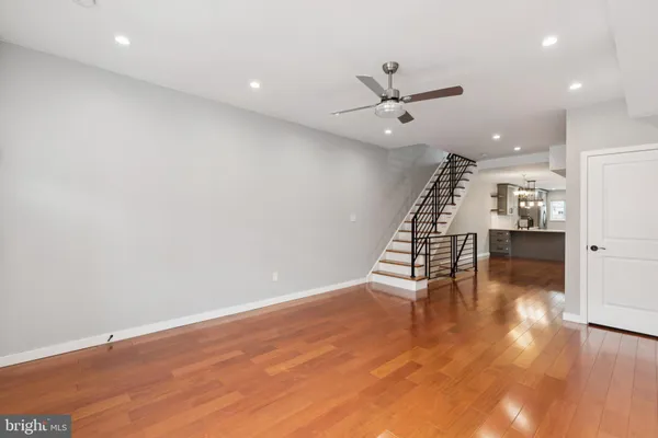 an empty room with wooden floor staircase and a kitchen
