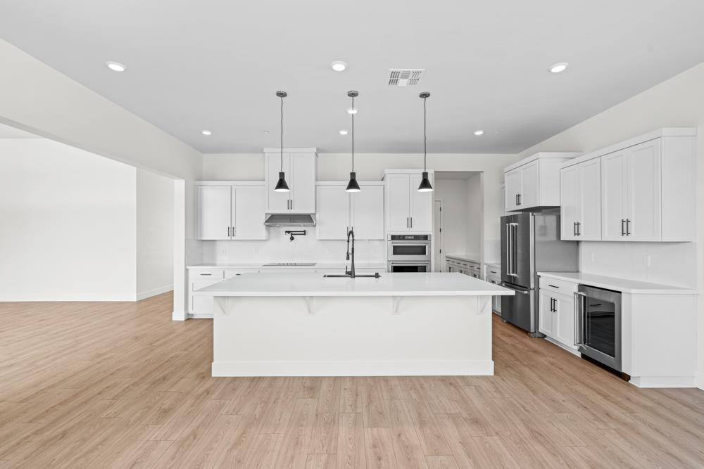 14854 Grace Warren Way Rancho Murieta, CA 95683 - Photo 11 of 27 a large white kitchen with kitchen island a stove a sink a refrigerator and white cabinets with wooden floor