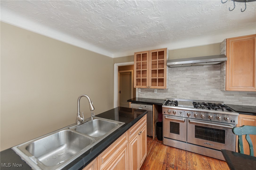 5062 Lee Road Maple Heights, OH 44137 - Photo 12 of 50 Kitchen featuring dark countertops, stainless steel appliances, wall chimney exhaust hood, light brown cabinets, and light wood finished floors