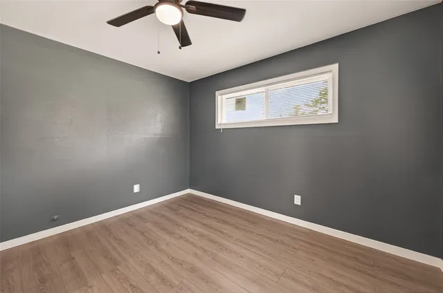an empty room with wooden floor ceiling fan and windows