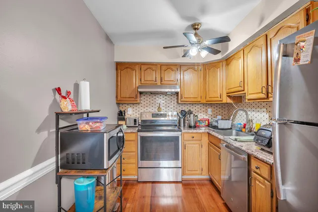 a kitchen with stainless steel appliances granite countertop a refrigerator a stove top oven a sink dishwasher and a dining table with wooden floor