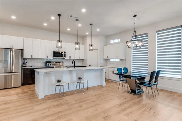 a kitchen with stainless steel appliances granite countertop a refrigerator a stove a sink dishwasher a dining table and chairs with wooden floor