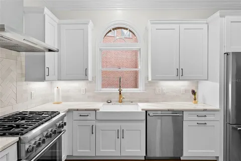 a large white kitchen with a refrigerator a sink dishwasher a stove and a dining table with wooden floor