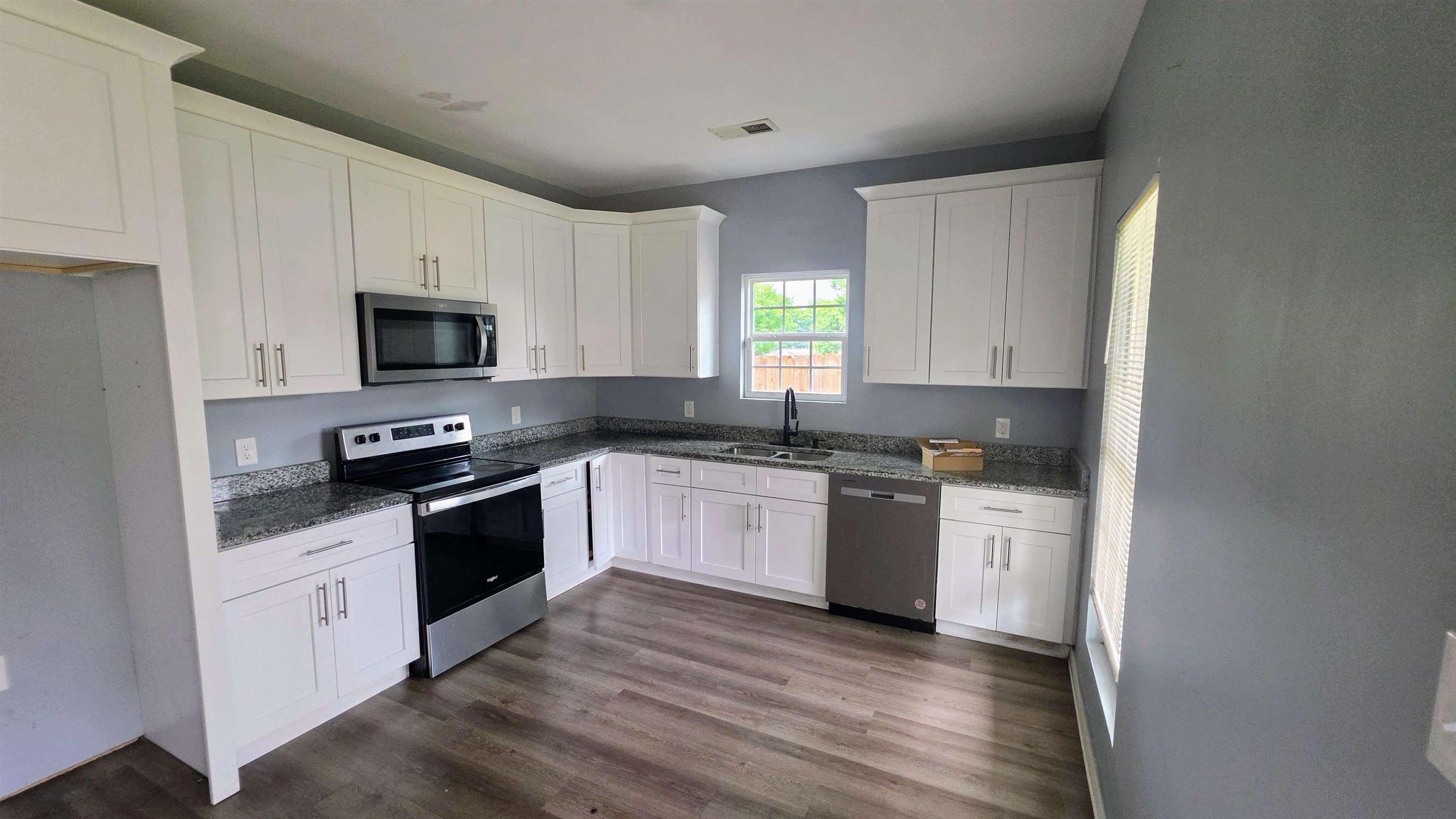 1551 Cane Road Memphis, TN 38106 - Photo 3 of 5 Contemporary kitchen featuring white cabinetry, stainless steel appliances, granite-style countertops, wood-finish flooring, and a window above the sink