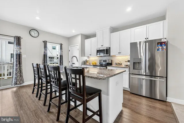 a kitchen with stainless steel appliances granite countertop a dining table chairs refrigerator and microwave