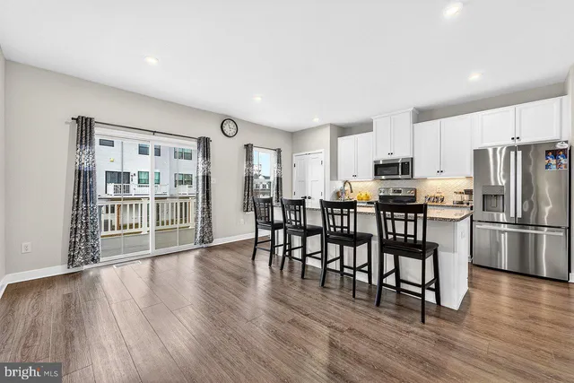 a kitchen with stainless steel appliances a dining table chairs refrigerator and cabinets