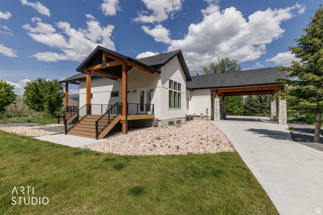 1188 South Old Trappers Loop Road Huntsville, UT 84317 - Photo 11 of 92 Modern farmhouse exterior featuring white vertical siding, a covered porch with wood posts, a wood-finish deck with black railings, a paved driveway, and an attached carport with stone pillars