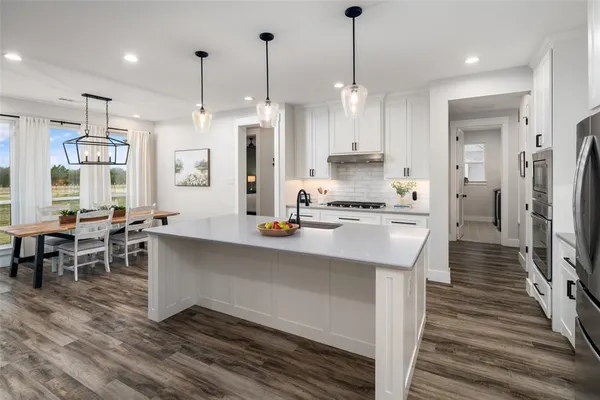 a large kitchen with stainless steel appliances kitchen island granite countertop a refrigerator a stove a sink and a dining table with wooden floor